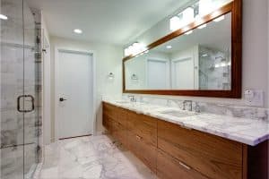 Modern bathroom with marble floors and countertops, a wooden double-sink vanity, large wall mirror, glass shower enclosure, and white walls with recessed lighting, creating a clean and elegant look—perfect for sophisticated Mercer Island living.