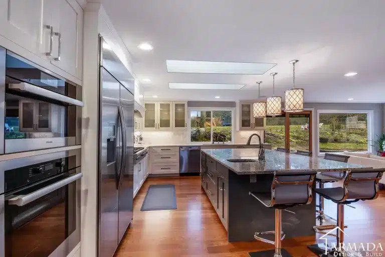 Modern kitchen with stainless steel appliances, large island with dark cabinets, granite countertop, barstools, pendant lights, white cabinets, wood floor, and large windows overlooking a green yard—perfect inspiration for anyone choosing kitchen cabinets or looking for ideas for new kitchen cabinets.
