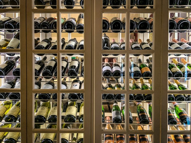 Bottles of wine stored horizontally on shelves behind a grid of glass panes, with labels visible and dim lighting highlighting the organized wine collection, create a sophisticated wine cellar that elevates any home design while reflecting both taste and an awareness of cost.