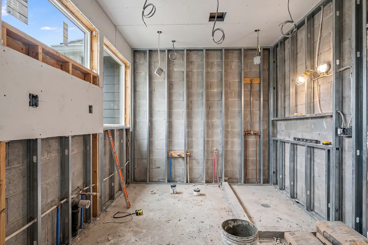 Bathroom during remodeling with open steel stud walls, exposed plumbing and a bare concrete floor