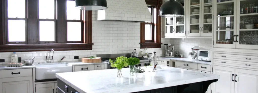 A kitchen with a large white marble-topped island, white subway tile backsplash, and white cabinetry.