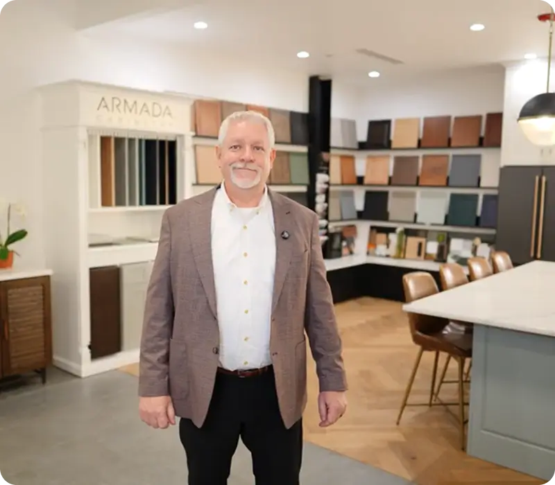 A man in a blazer stands in a showroom featuring displays of cabinet finish samples.