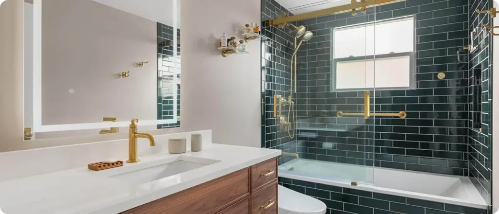 Modern bathroom with a white countertop, wooden vanity, gold fixtures, backlit mirror, dark green tile shower, and glass doors—perfect for Aging in Place Remodeling in the Greater Seattle Area.